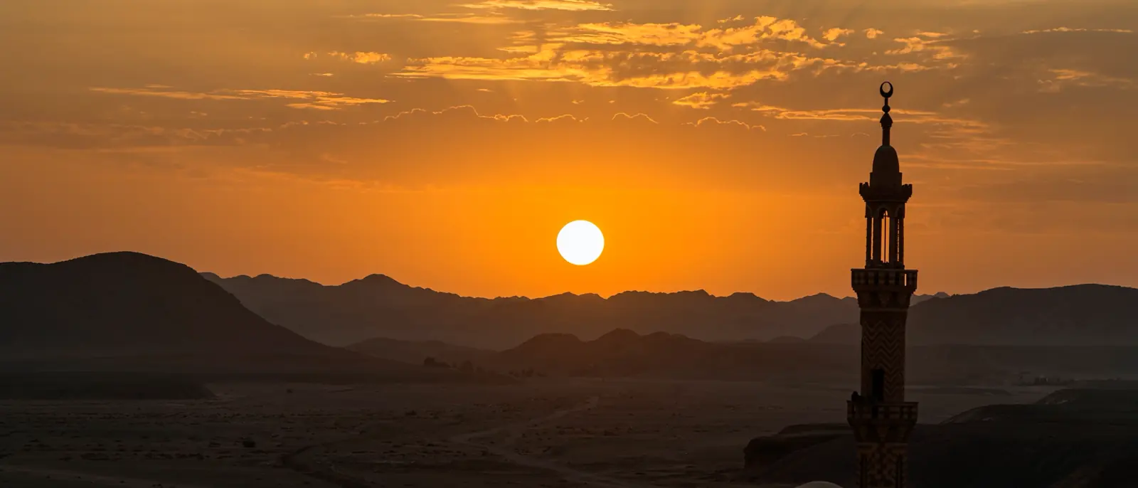 غروب الشمس خلف الجبال بجوار مئذنة مسجد